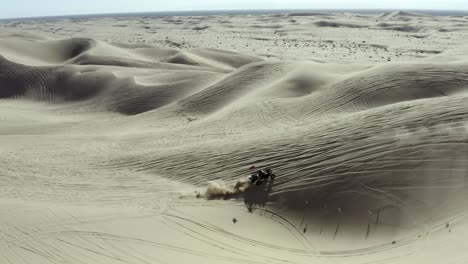 All-terrain-vehicle-ATV-driving-over-sand-dunes-in-desert,-aerial-view