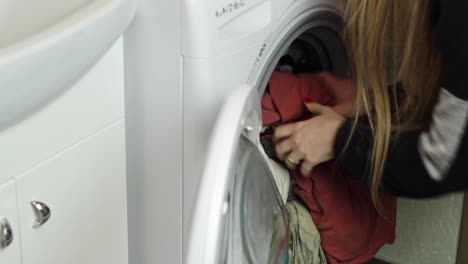 Static-view-of-a-woman-opening-and-unloading-a-washing-machine-load-into-a-basket-underneath