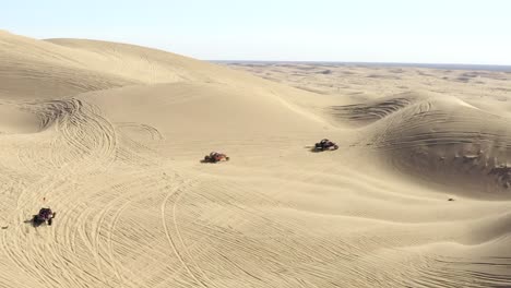 Aerial-follow-view,-all-terrain-vehicles-ATVs-in-desert-driving-over-sand-dunes