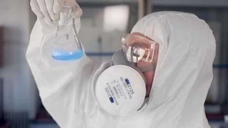 Wissenschaftler-In-Einem-Schutzanzug-Und-Einem-Atemschutzgerät-Untersucht-Eine-Blaue-Substanz-In-Einem-Reagenzglas