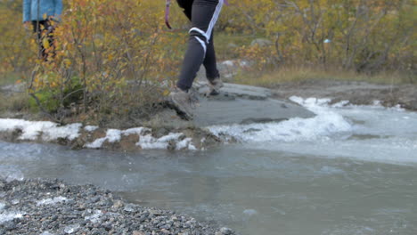 A-Woman-in-Boots-Running-and-Jumping-Across-an-Icy-Stream-in-Norway,-Slow-Motion
