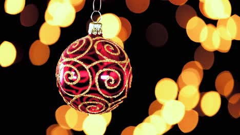 single-red-clear-Christmas-ball-ornament-with-golden-glitter-stripes-and-out-of-focus-lights-flickering-in-the-background,-close-up