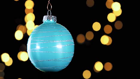 Einzelne-Blaue-Türkisfarbene-Weihnachtskugel-Mit-Glitzerstreifen-Und-Unscharfen-Lichtern,-Die-Im-Hintergrund-Flackern,-Nahaufnahme