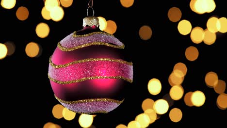 single-red-Christmas-ball-ornament-with-golden-silver-glitter-stripes-and-out-of-focus-lights-flickering-in-the-background,-close-up