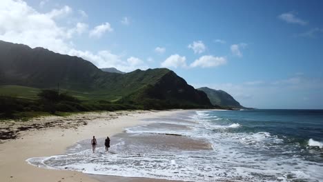 People-enjoying-walking-on-the-white-sand-Makua-Beach-by-the-green-mountains-of-Oahu,-Hawaii---aerial