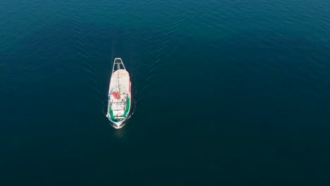 Aerial-top-down-view-of-fishing-boat-sailing-in-deep-blue-sea,-sunny-day