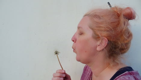 Woman-stands-near-wall-blowing-dandelion-seeds-away,-profile,-close-up