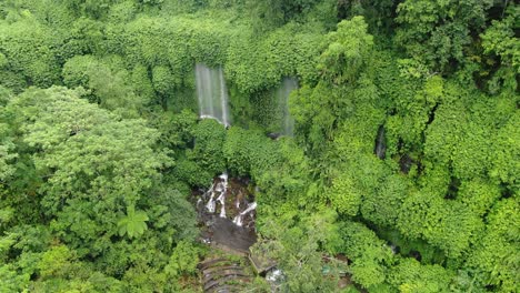 Flying-in-shot-to-a-beautiful-hidden-waterfall-in-a-tropical-rainforest-in-Asia,-lush-green-environment-fro-above