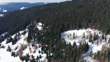 Increíbles-Montañas-Y-árboles-Cubiertos-De-Nieve-Invernal-Con-Una-Pequeña-Cabaña-En-El-Medio,-Retroceso-Aéreo-De-Drones-De-Navidad