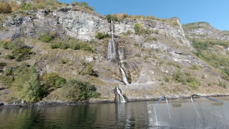 Blick-Von-Einem-Boot-Auf-Einen-Hohen-Wasserfall,-Der-Von-Einem-Berg-In-Einen-Fjord-Fließt
