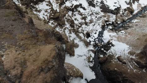 Drohne-Fliegt-über-Eiskaltes-Flusswasser-Und-Schneebedeckten-Felsen-In-Island---Drohne