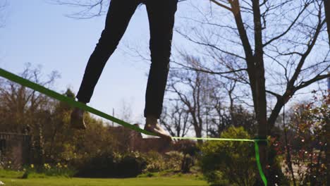Low-angle-of-barefoot-young-man-attempting-to-slack-line-then-loosing-balance-and-falling-off