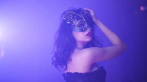 Young-broken-woman-with-a-mask-on-red-lipstick-corset-surrounded-by-blue-and-purple-light-slowmotion
