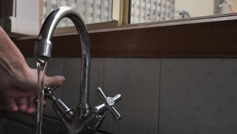 Person-hand-reaching-in-a-turning-water-on-and-off-in-traditional-kitchen-sink-with-hand-staying-on-tap