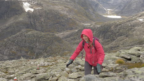 A-Woman-Smiles-as-She-Hikes-up-a-Steep-Rocky-Landscape-on-a-Cold,-Overcast-Day-in-Norway