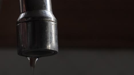 Water-turned-on-trickling-out-of-kitchen-sink-tap-before-turned-off-and-dripping-slowly-from-metallic-spout