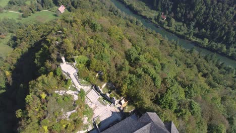 High-angle-aerial-revealing-Kostel-Castle-on-a-hill-beside-Kolpa-river,-Slovenia