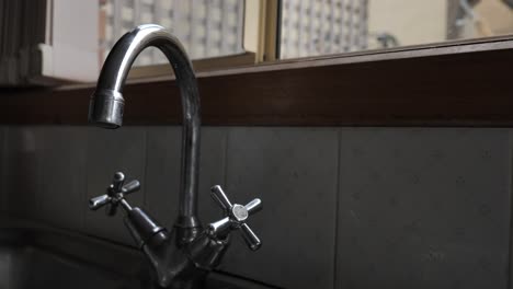 Metallic-silver-tap-dripping-then-leaking-slowly-in-traditional-home-kitchen-sink-with-hot-and-cold-taps
