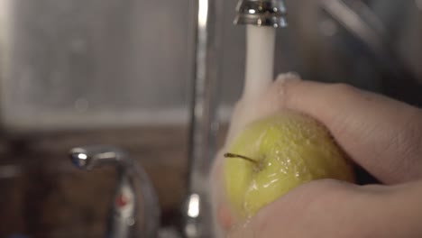 Einen-Kleinen-Gelben-Apfel-Mit-Zwei-Händen-Unter-Dem-Wasserhahn-Waschen