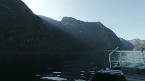 Ein-Rippenboot-Rast-Sanft-über-Einen-Fjord-In-Norwegen-In-Richtung-Sonnenstrahlen,-Die-über-Einen-Berggipfel-Ziehen