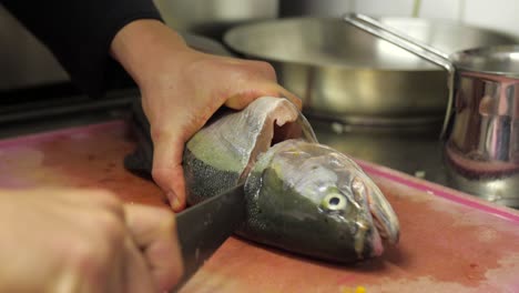 Chef-Cortando-La-Cabeza-De-Un-Pez-Trucha-De-Mármol-Con-Un-Cuchillo-Grande-En-Una-Tabla-De-Cortar