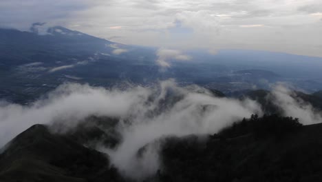 Mysteriöse-Luftaufnahme,-Die-über-Nebelverhangene-Berge-Fliegt,-Weiße-Wolken-Bei-Sonnenaufgang,-Eine-Schlafende-Stadt-Im-Tal-Im-Morgengrauen