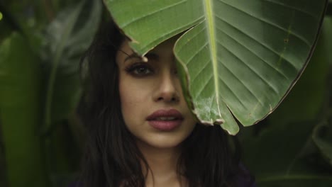 Young-Indian-female-woman-hiding-behind-a-large-leaf-in-greenhouse