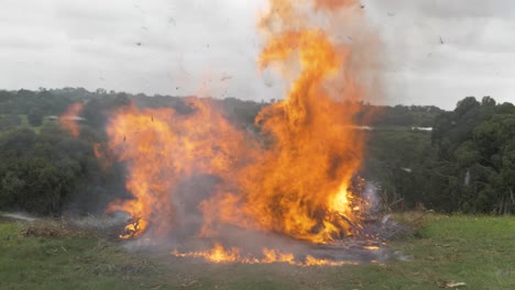 A-slow-motion-shot-of-a-large-bonfire-on-a-rural-property-with-ash-flying-everywhere
