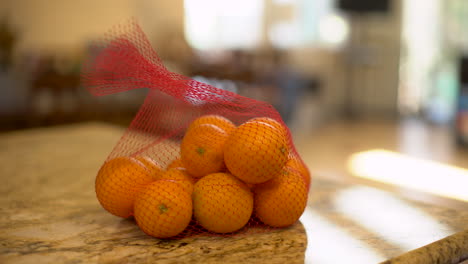 Tripod-shot-of-a-man-dropping-a-bag-of-oranges-on-a-kitchen-counter-on-a-warm,-sunny-day