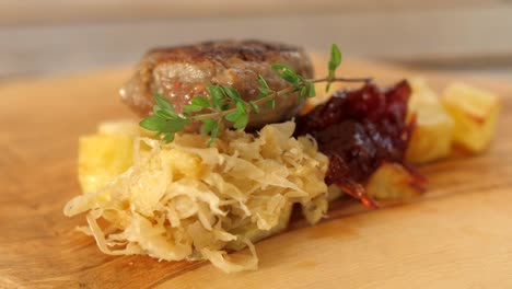 Chef-puts-rosemary-branch-on-plate,-beef-burger,-cabbage,-cranberry-jam-and-roasted-potatoes-served-on-wooden-board