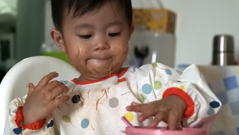 Adorable-asian-baby-girl-playing-with-spoon-and-food-after-eating-at-home