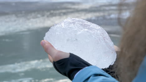 A-Woman-Holds-a-Large-Chunk-of-Ice-Next-to-a-Glacial-River-in-Norway,-Close-Up-Slow-Motion