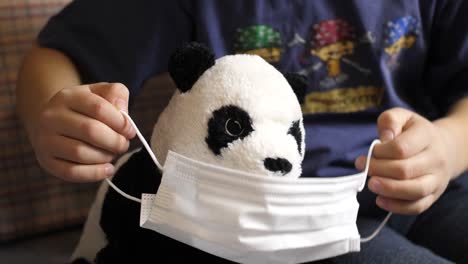 Young-Caucasian-boy-puts-mask-on-stuffed-baby-panda,-Covil-19-quarantine