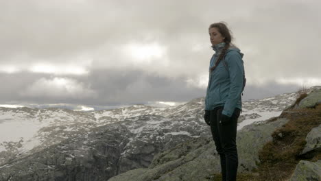 Eine-Frau-Nimmt-An-Einem-Windigen,-Bewölkten-Tag-In-Norwegen,-Zeitlupe,-Einen-Schneebedeckten-Und-Felsigen-Blick-Von-Einem-Hochgelegenen-Berg-Auf