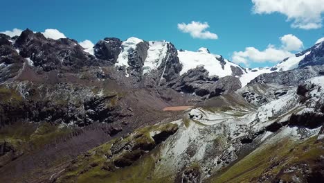 Aéreo,-En-Ascenso,-Disparo-De-Drones-Hacia-Un-Lago-Marrón,-En-Medio-De-Picos-Nevados,-En-Las-Montañas-Andinas,-Cielo-Azul,-En-La-Región-De-Cusco,-Perú