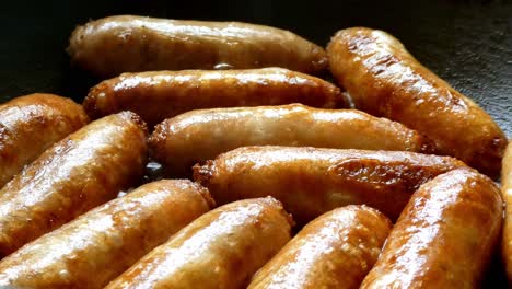 Sausages-frying-in-hot-pan-cooking-golden-delicious-grilled-meat-top-view-close-up
