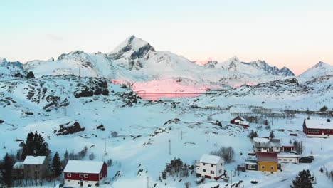 Drone-view-of-a-small-town-during-the-Winter-in-the-Lofoten-Islands-and-the-sunrise-in-the-fjord-at-the-background-with-the-mountains