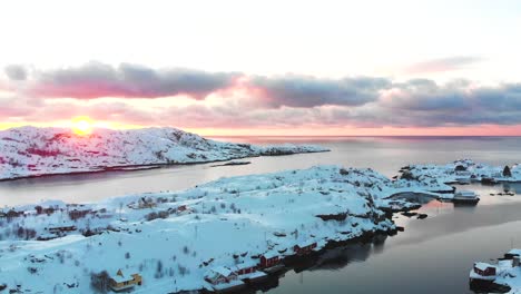 Drone-view-of-a-snowy-landscape-on-the-Lofoten-Islands-with-the-sunrise-at-the-background-and-some-clouds