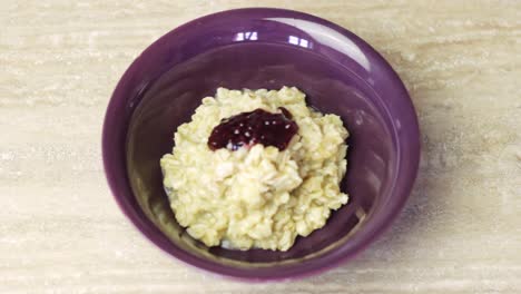 Using-a-teaspoon-to-add-raspberry-jam-to-a-bowl-of-steaming-hot-oatmeal-to-add-flavor
