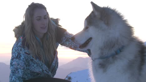 Pretty-smiling-young-woman-caressing-big-fluffy-dog-in-mountains,-sunset-slowmo