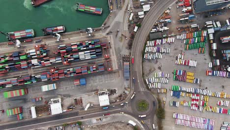 Large-Container-Ship-docked-at-Hong-Kong-commercial-port,-top-down-aerial-view-including-Stacks-of-Shipping-containers-on-a-holding-platform
