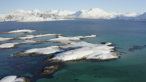 Vista-Aérea-De-Pequeñas-Islas-Cubiertas-De-Nieve-En-El-Océano-ártico-Con-Un-Hermoso-Paisaje-Invernal-En-El-Fondo