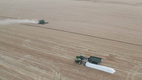 Static-aerial-view-of-single-combine-harvester-with-harvest-support-equipment-in-the-foreground