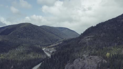 aerial-hold-overlooking-a-highway-freeway-interstate-inbetween-a-thick-forest-covered-mountain-valley-on-a-party-cloudy-blue-sky-summer-day-with-a-rocky-cliff-hwy2-2