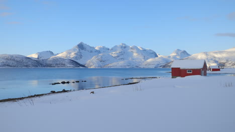 A-Bright-Red-Barn-on-the-Snowy-Shore-of-a-Calm-Lake-with-Amazing-Snow-Covered-Mountains-in-the-Background,-Static