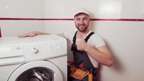plumber-in-work-uniform-hooked-up-the-washing-machine-and-shows-thumb-up-that-everything-is-fine