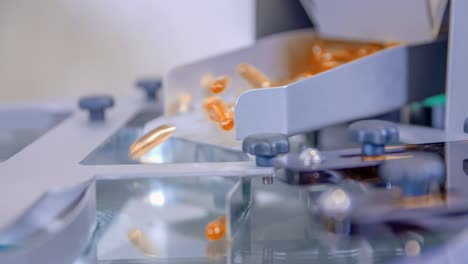 Orange-gel-capsules-falling-into-a-machine-in-the-pharmaceutical-lab