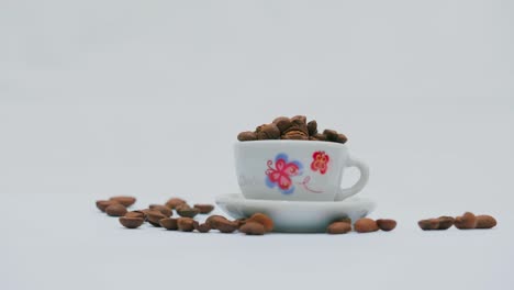 Studioaufnahme:-Kaffeebohnen-In-Und-Um-Eine-Weiße-Tasse-Und-Untertasse-Mit-Blumenmuster