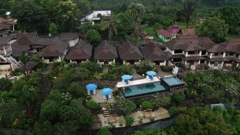 Orbital-aerial-shot-over-a-luxury-villa-complex-in-Asia,-a-man-standing-at-the-swimming-pool-surrounded-by-a-tropical-forest
