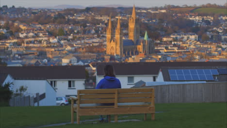 Person-sits-on-park-bench-looking-over-Truro,-UK-and-iconic-cathedral,-wide